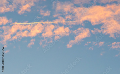 View of early morning sky with soft pink clouds and steam chem trails left by airplane.