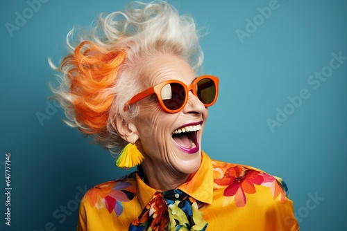 A delighted senior woman, dressed in a vibrant orange outfit and stylish sunglasses, enjoys hearty laughter and fun in a fashion studio.
