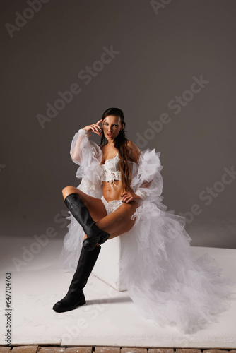 Beautiful woman in white fluffy fur coat and boots in studio. Long-haired brunette girl in lace pants. Gorgeous big lips and eyes. Portrait of pretty woman.  Woman in  white underwear