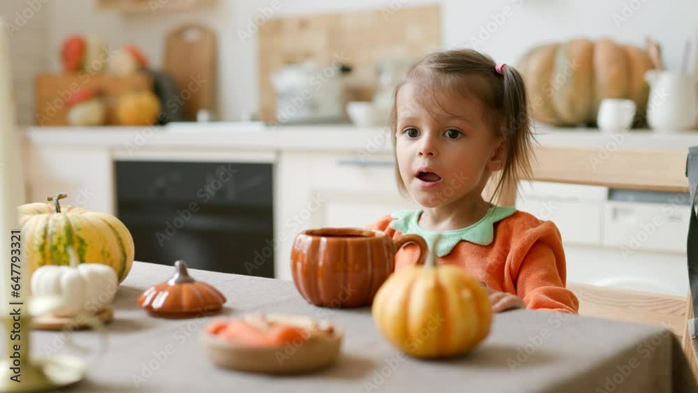 Happy Halloween! Little cute girl eating in the kitchen. Toddler girl in a pumpkin costume eating sandwiches on breakfast. Morning at home. Happy Halloween! Little cute girl eating in the kitchen. Toddler girl in a pumpkin costume eating sandwiches on breakfast. Morning at home.