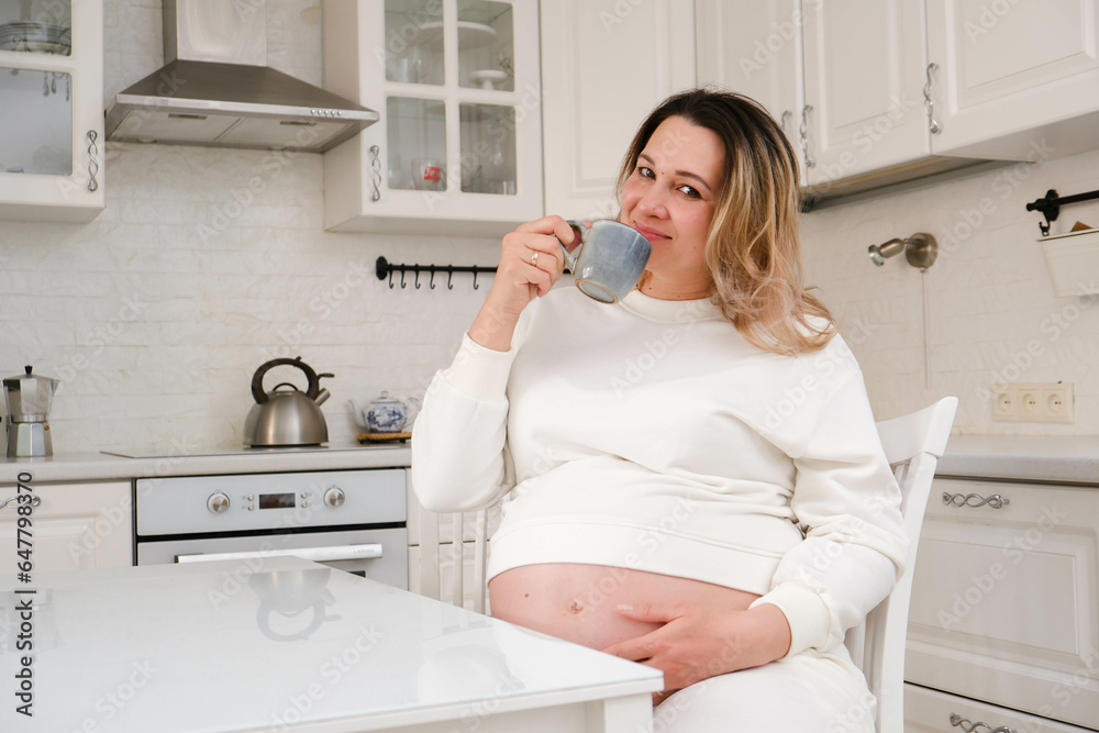 Beautiful pregnant woman is drinking tea in light kitchen. Beautiful pregnant woman is drinking tea in light kitchen.