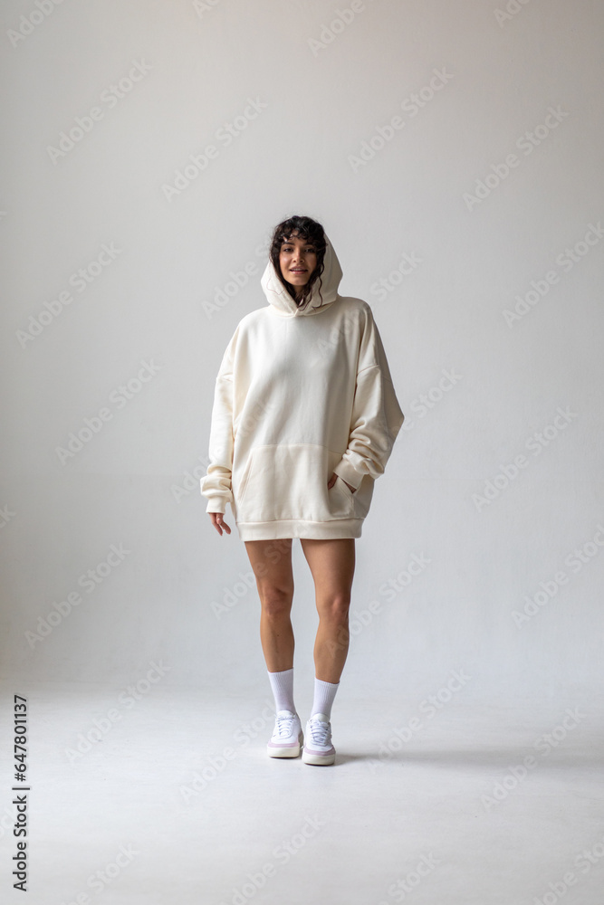 Brunette woman with curly hair in a white oversized hoodie and bare legs. Brunette woman with curly hair in a white oversized hoodie and bare legs.