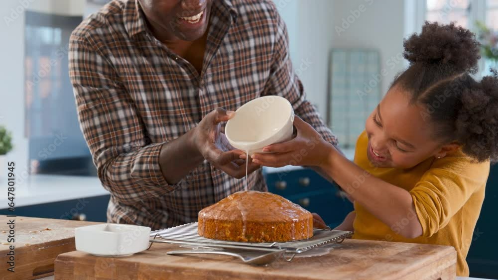 Father and daughter baking at home in kitchen decorating homemade cake with icing - shot in slow motion