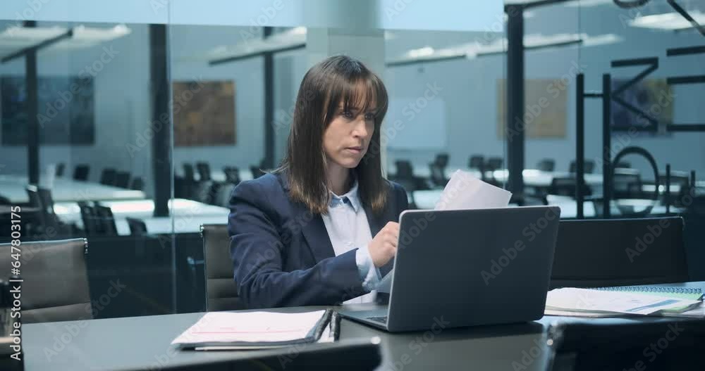 Within the office environment, a Caucasian woman is immersed in her work with papers. Her focused attention on the documents before her reflects her commitment to thoroughness.