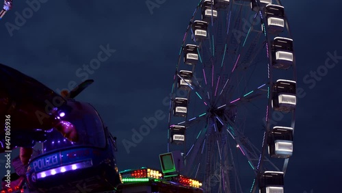 modern ferris wheel with closed cabins at carnival with blue sky no clouds in the background illuminated wide angle close up shot