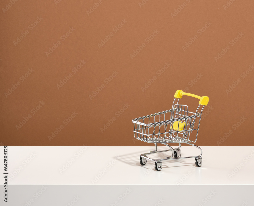 The shopping cart stands on a brown background. Copy space for text. Idea of weekend shopping.