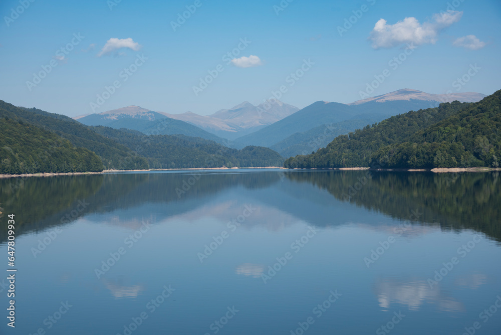 Smooth lake surface with beautiful reflection of cloudy sky and the hills are covered with dense forest