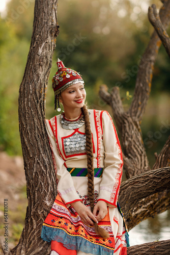 a girl in a Chuvash national costume on a tree on the shore of a forest pond