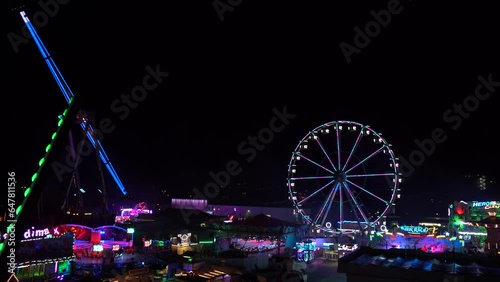modern ferris wheel with closed cabins at carnival with blue sky no clouds in the background illuminated wide angle close up shot