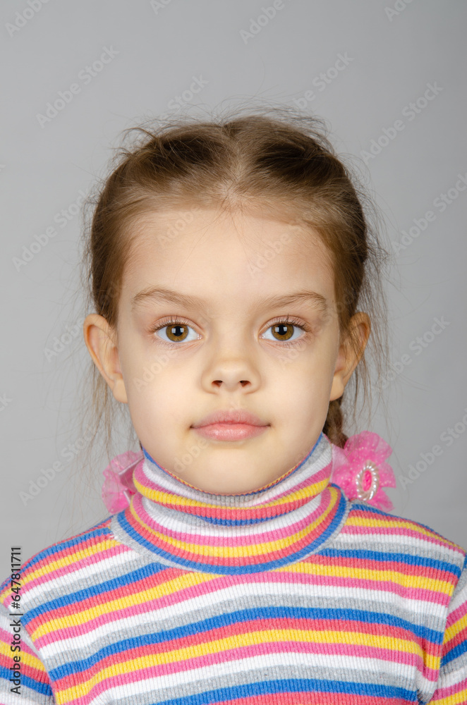 Close-up portrait of a disheveled five-year-old girl wearing a colored striped sweater on a gray background Close-up portrait of a disheveled five-year-old girl wearing a colored striped sweater on a gray background