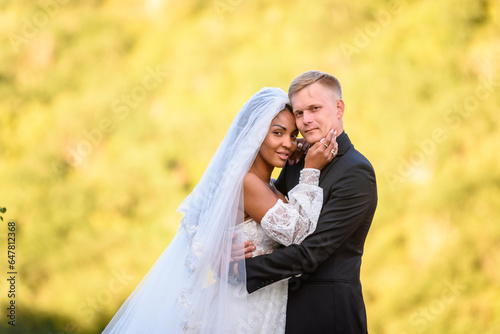 Happy newlyweds against the background of evening sunny foliage, the couple looks into the frame