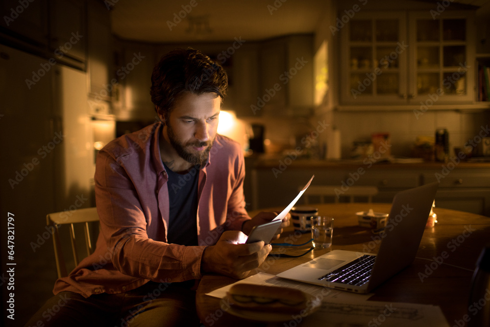 Young Caucasian man using a smartphone while going over his bills and home finances at night at home Young Caucasian man using a smartphone while going over his bills and home finances at night at home