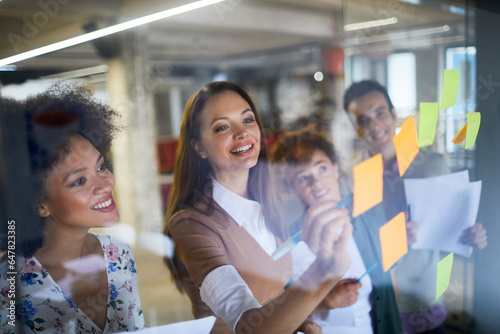 Young and diverse group of people going over ideas for a project and putting notes on a window in a startup company office