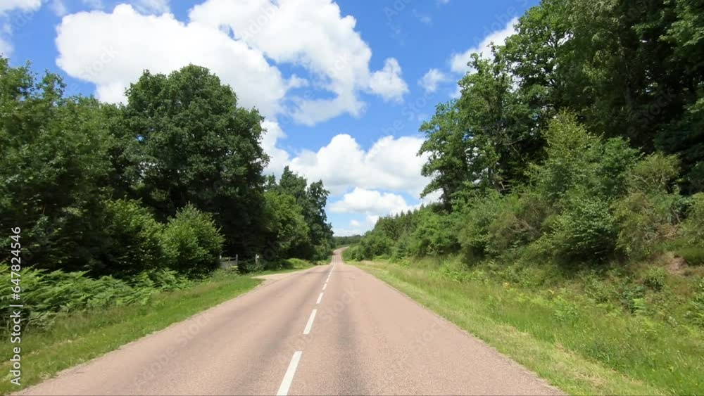 A road crosses the green countryside and its wheat fields in Europe, in France, in Burgundy, in Nievre, towards Chateau Chinon, in summer, on a sunny day. A road crosses the green countryside and its wheat fields in Europe, in France, in Burgundy, in Nievre, towards Chateau Chinon, in summer, on a sunny day.