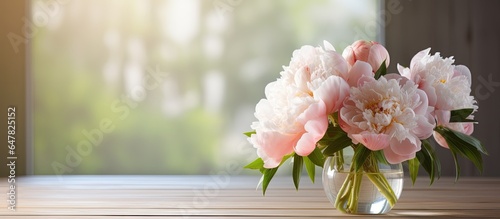 Pale peonies arranged in a glass vase on a wooden table