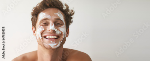 Obraz na plátně Portrait of a laughing young man smeared face with facial moisturizer cream