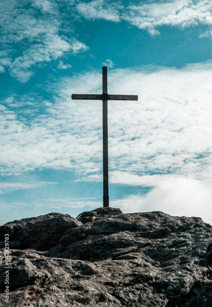 Naklejka premium Vertical shot of the cross on the top of the stony hill against a blue sky