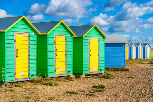 Colorfool beach huts on the shores of Littlehampton East Beach in Sussex, England, UK; wooden yellow, green and blue huts on pebbles beach