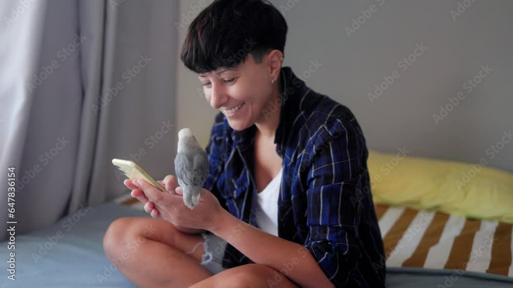 Parrot bird and young woman having fun using mobile phone at home - Owner and exotic animal friendship and domestic life concept Parrot bird and young woman having fun using mobile phone at home - Owner and exotic animal friendship and domestic life concept
