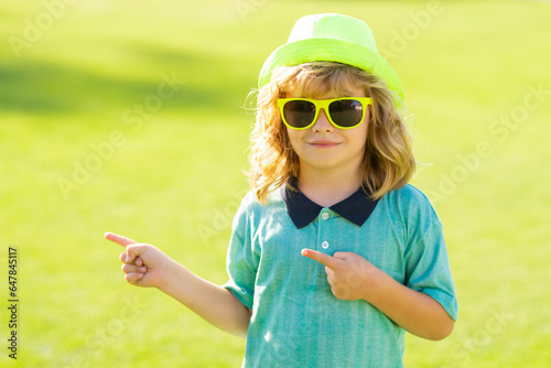 Kid point finger. Lifestyle portrait of funny kid outdoors. Summer kids outdoor portrait. Close up face of cute child. Kid having fun outdoor on sunny summer day.