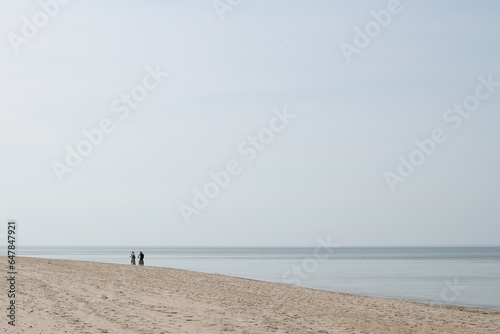 Pusta plaża morska. Dwie osoby spacerują w słoneczny dzień brzegiem morza. Złota polska jesień nad morzem.