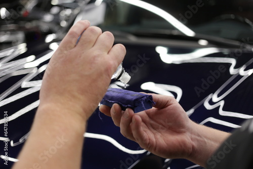 Automotive ceramics. Car service worker applying nano coating on a car detail close-up. Closeup of hand coating green car bonnet paint. 