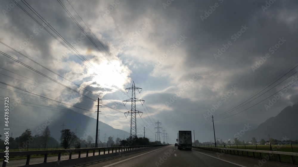 A truck cruises along a highway beneath a cloudy sky, its rumbling engine echoing through the mist.