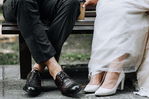 Legs with shoes close-up of the bride and groom sitting on a park bench. Wedding photography of the newlyweds, portrait.