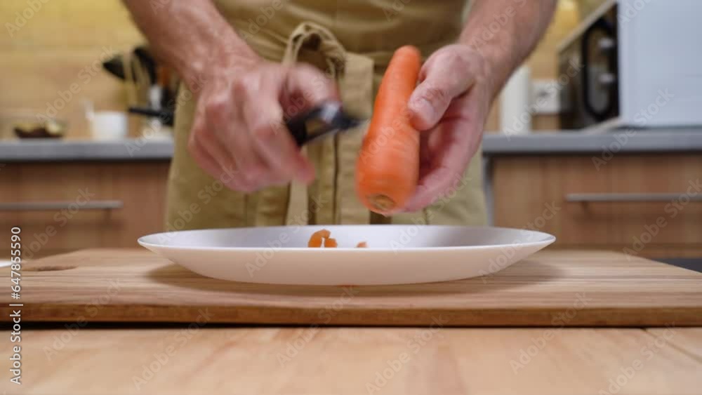 A man in an apron peel a carrot with a special knife. A man in an apron peel a carrot with a special knife.