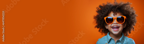 Portrait happy smiling African-American elementary school toddler boy in sunglasses, blue shirt on orange studio background. Positive emotions of coming school autumn time. Place for text, copy paste