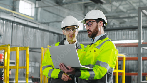 Main engineer briskly explains plan of action to employee. Bearded man holding notebook and gesturing. Workers in yellow jackets and helmets cooperate at construction site. photo