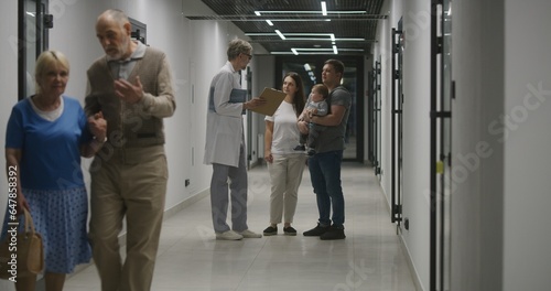 Doctor and family with little child stand in clinic corridor. Doctor talks to patients, discusses medical examination or test results. Medical staff and people in hospital, medical center. Healthcare.