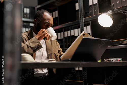 Photo African american cop drinking coffee and reading csi report at night time