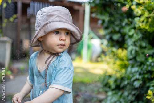 Cute baby boy plays with water in garden 