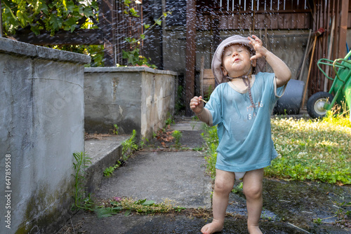 Cute baby boy plays with water in garden 