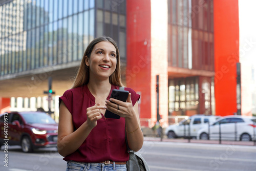 Brazilian business woman using her smartphone with ring holder walking on Paulista Avenue in Sao Paulo megalopolis, Brazil photo