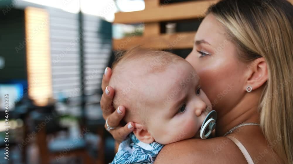 Blonde woman is holding her baby boy. Mother is calming her infant with pacifier in mouth. Close up. Blonde woman is holding her baby boy. Mother is calming her infant with pacifier in mouth. Close up.