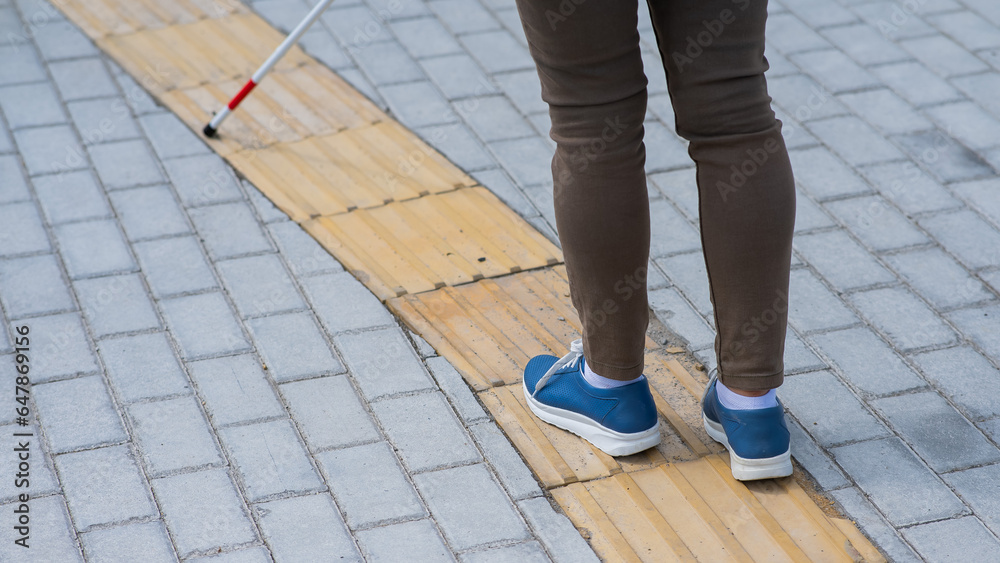 Close-up of a woman's legs with a cane near a tactile tile. Close-up of a woman's legs with a cane near a tactile tile.