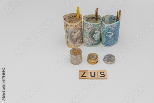 Banknotes arranged in a roll with 3 denominations of 50 zloty 100 zloty and 200 zloty next to which lie coins and zus wood inscription. The concept of early retirement, increasing the value of contrib photo