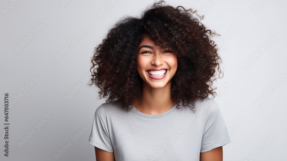 Smiling woman with curly afro hair, wearing a hat, exudes joy and confidence in a studio portrait