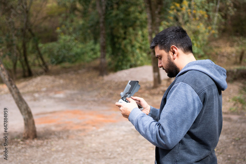 Male person using the remote control of a drone in an environment with green trees.