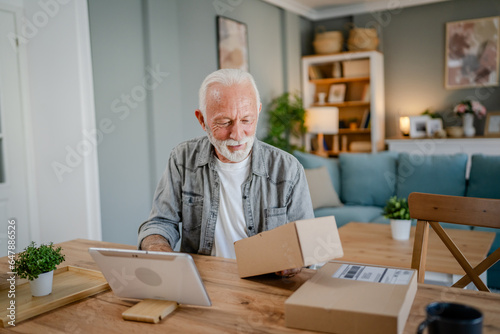 senior man sit at home hold post package delivery use digital tablet