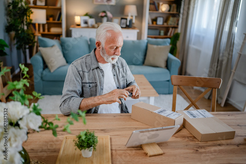 senior man sit at home hold post package delivery use mobile phone
