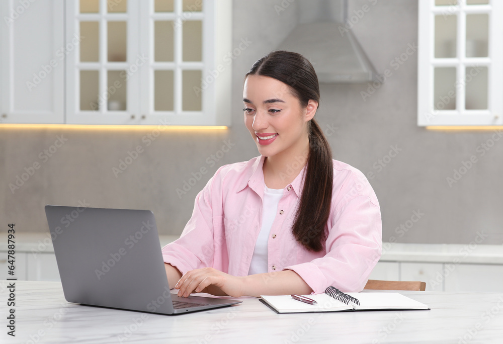 Woman using laptop at white table in kitchen Woman using laptop at white table in kitchen