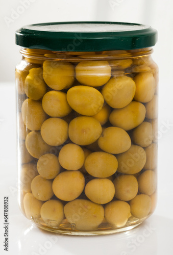 Glass jar with delicious pickled whole olives on white background..