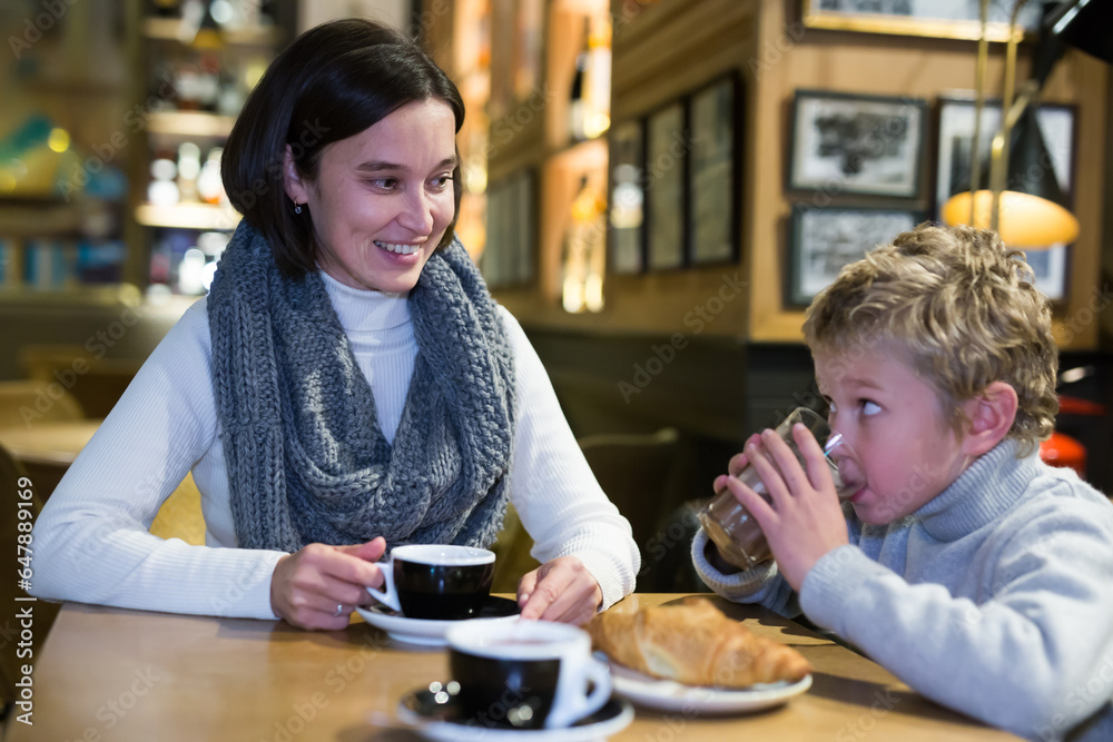 Happy woman enjoying communication with her preteen son while visiting cozy cafe..
