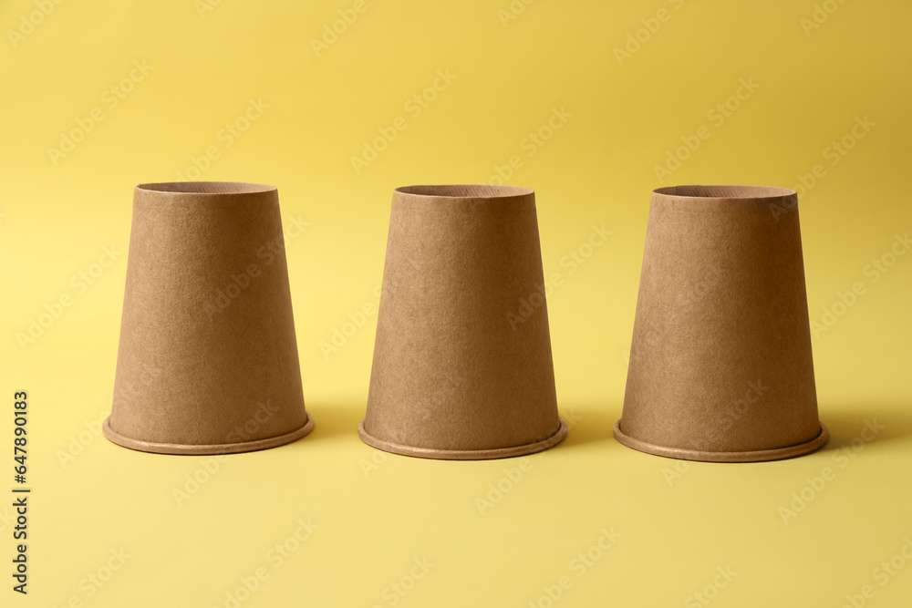 Three paper cups on yellow background. Thimblerig game Three paper cups on yellow background. Thimblerig game