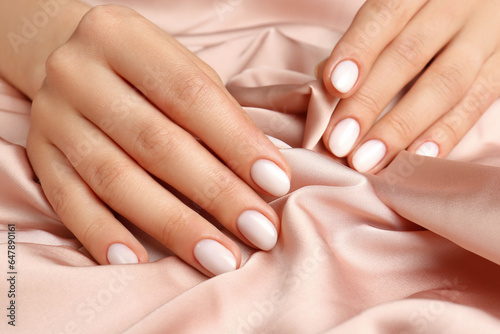 Woman showing her manicured hands with white nail polish on beige silk fabric, closeup