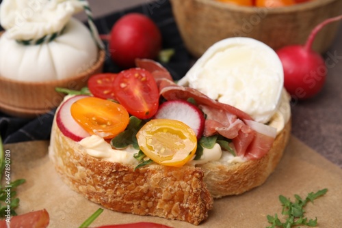 Delicious sandwich with burrata cheese, ham, radish and tomatoes on table, closeup