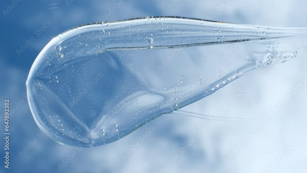 Female hand using spatula applies smear of shampoo or shower gel against the background of sky and clouds, top view.